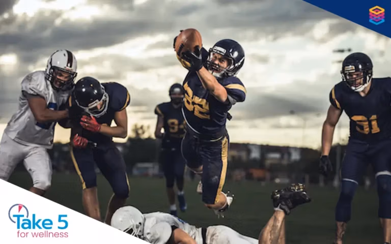 Time to tackle wellness tax barriers - American football player catching a football while leaping over an opponent - Benefits Alliance